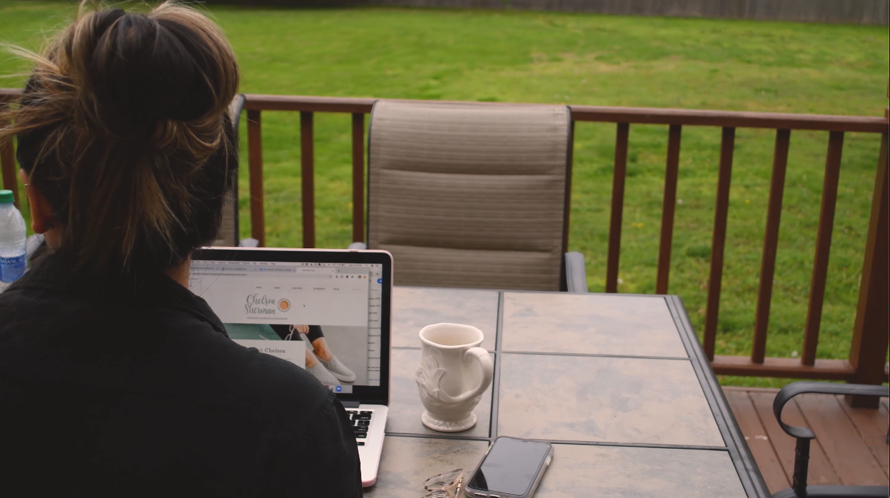 woman facing away sits at a computer on an outdoor deck