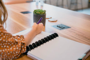woman's hand writing in notebook on wood desk